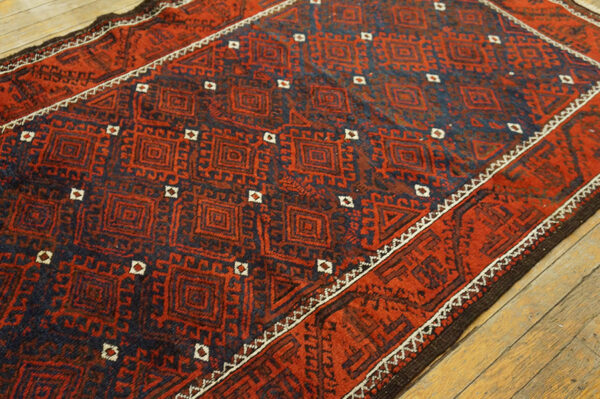 Red and navy geometric rug featuring repeating squares rests on light brown hardwood flooring.