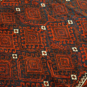 Red and dark blue rug with dense, repeating geometric diamond and square motifs.