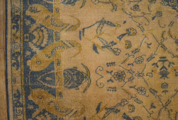 Distressed, low-pile rug detail in tan and dark blue with stylized floral patterns on wood flooring.