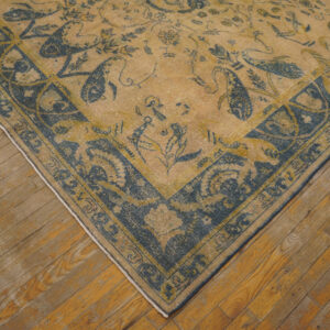 Low-pile beige rug with dark blue traditional motifs and borders sits on rustic wood plank flooring.