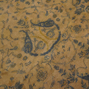 Low-pile tan rug featuring large dark blue paisley and detailed scrolling floral patterns with yellow accents.
