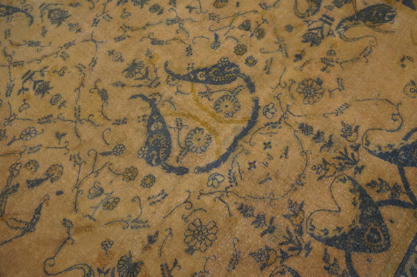 Low-pile tan rug featuring large dark blue paisley and detailed scrolling floral patterns with yellow accents.
