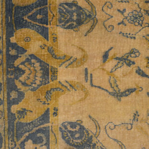 Low-pile rug detail showing gold, navy, and yellow stylized birds and floral designs on wood flooring.