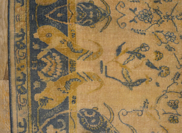 Low-pile rug detail showing gold, navy, and yellow stylized birds and floral designs on wood flooring.