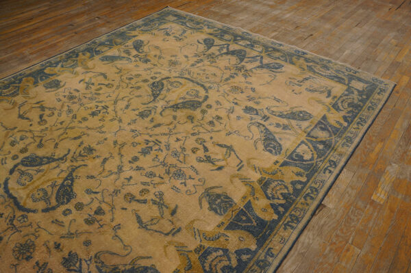 Low-pile gold and indigo traditional rug featuring floral and bōteh patterns on plank wood flooring.