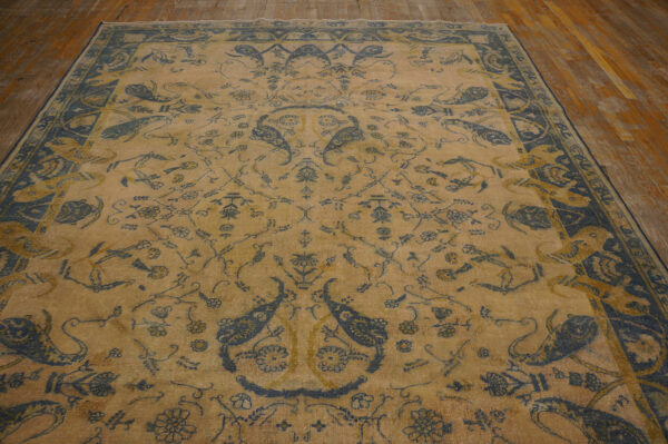 Distressed tan rug with detailed blue and yellow traditional patterns covering a wood plank floor.