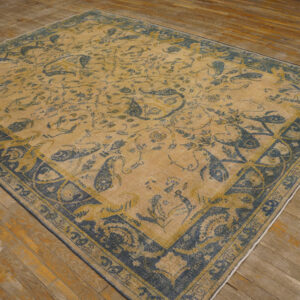 Distressed tan and indigo rug with detailed paisley motifs rests on worn hardwood flooring.