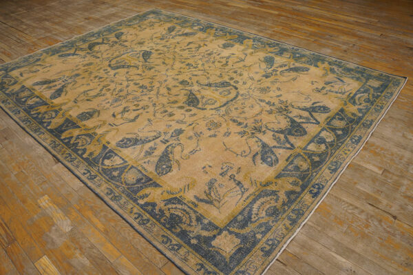 Distressed tan and indigo rug with detailed paisley motifs rests on worn hardwood flooring.