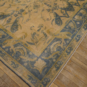 Muted tan rug with blue stylized animal and floral patterns lies on rustic wooden flooring.