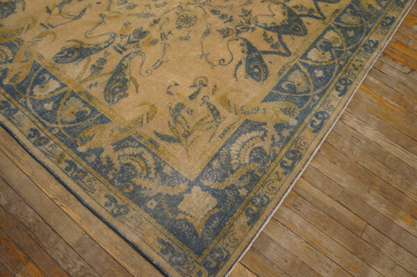 Muted tan rug with blue stylized animal and floral patterns lies on rustic wooden flooring.