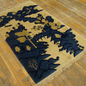 A tan rug with deep blue stylized mountains and trees lies on light hardwood flooring.