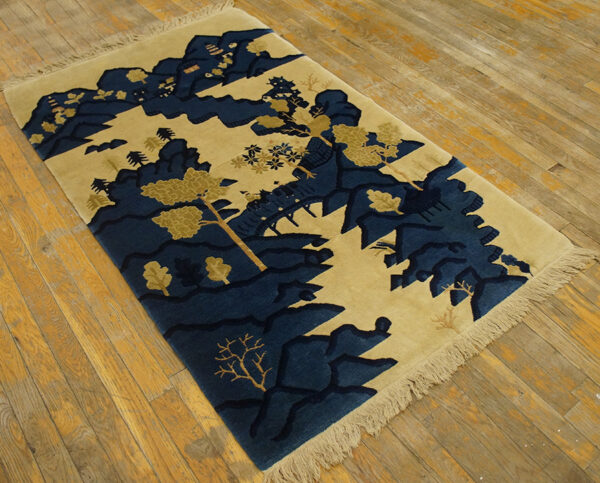 A tan rug with deep blue stylized mountains and trees lies on light hardwood flooring.