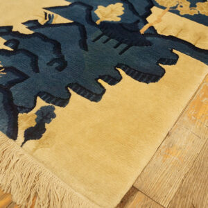 A textured tan rug with deep blue abstract patterns and visible fringe rests on wooden planks.