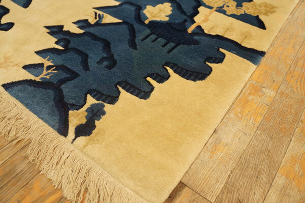 A textured tan rug with deep blue abstract patterns and visible fringe rests on wooden planks.