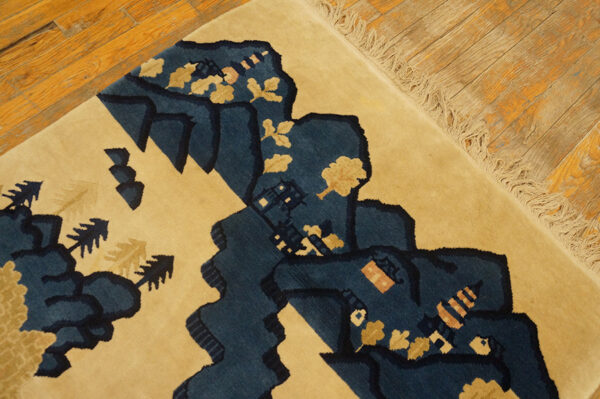 Close-up of a high-pile tan rug featuring a navy landscape design on rustic hardwood flooring.