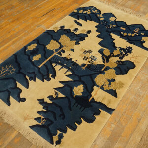 Beige and dark blue scenic landscape rug with fringe, laid diagonally on distressed wooden floorboards.