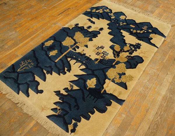 Beige and dark blue scenic landscape rug with fringe, laid diagonally on distressed wooden floorboards.