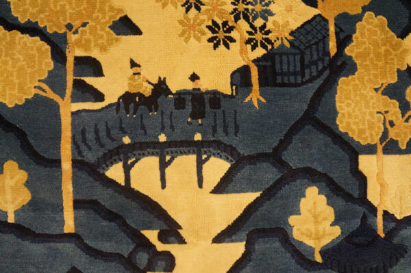 Blue and yellow scenic rug depicting trees, hills, a bridge, and two figures.