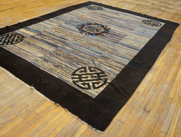 Dark bordered rug with blue, beige, and brown striped field and black medallions on light wood flooring.