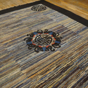 The striated blue and brown rug has a thick black border and black circular medallions on wood flooring.