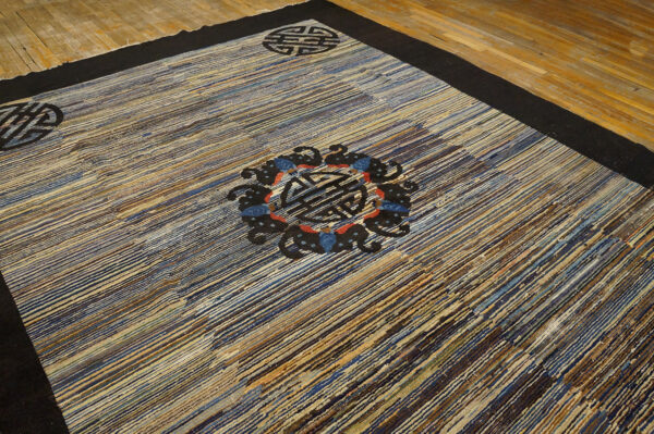 The striated blue and brown rug has a thick black border and black circular medallions on wood flooring.