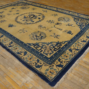 Golden rug with dark blue borders and medallions featuring floral and dragon designs on wood plank flooring.