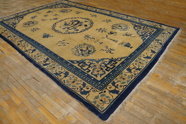 Golden rug with dark blue borders and medallions featuring floral and dragon designs on wood plank flooring.