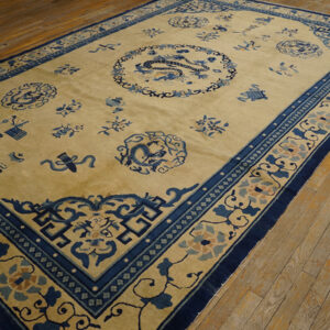 Tan field rug with intricate navy blue borders and central dragon pattern covers light wood flooring.