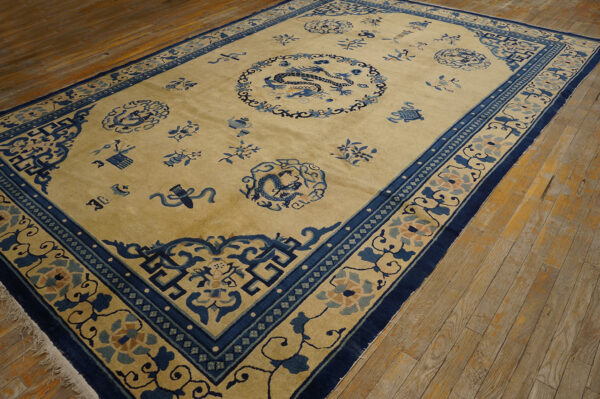 Tan field rug with intricate navy blue borders and central dragon pattern covers light wood flooring.