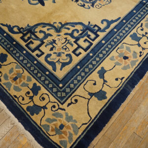 Beige rug corner with deep blue borders and stylized floral motifs rests on light wood planks.