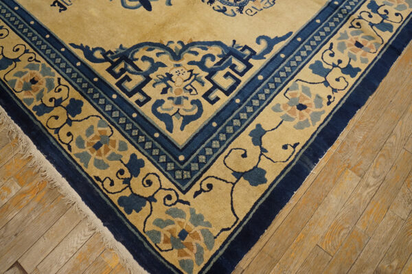 Beige rug corner with deep blue borders and stylized floral motifs rests on light wood planks.