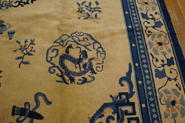 Close view of a tan rug with dark blue dragon, plant motifs, and multicolored floral borders.