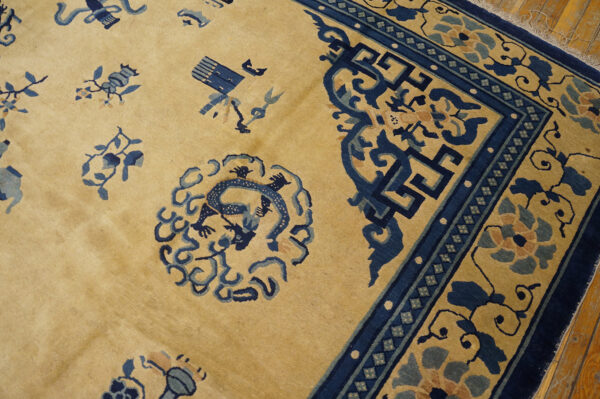 Tan rug featuring a dark blue border, scattered florals, and a central mythical figure motif on wood flooring.