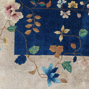 High-pile rug corner showing a vibrant blue field and beige border with winding multicolored floral designs.