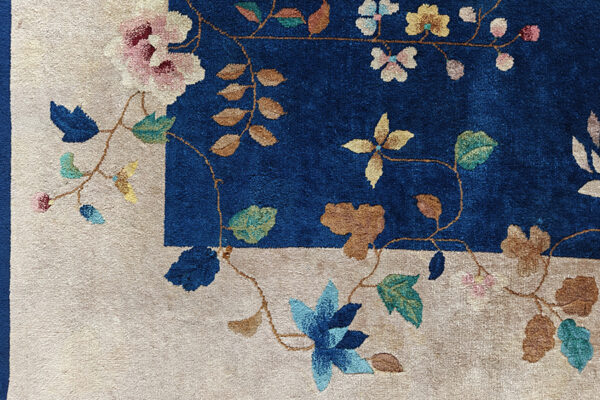 High-pile rug corner showing a vibrant blue field and beige border with winding multicolored floral designs.