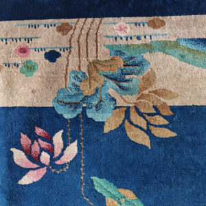 Deep blue rug detail with a beige band, featuring stylized botanical motifs in pink, turquoise, and tan.