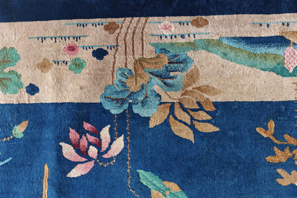 Deep blue rug detail with a beige band, featuring stylized botanical motifs in pink, turquoise, and tan.