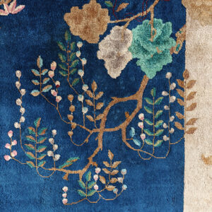 Blue rug with high pile texture featuring botanical patterns in teal, tan, and pink, bordered by cream.