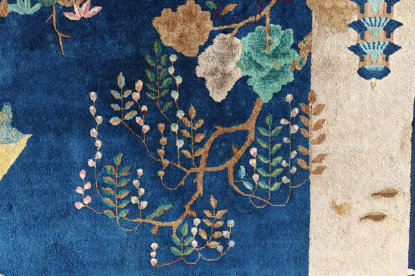 Blue rug with high pile texture featuring botanical patterns in teal, tan, and pink, bordered by cream.