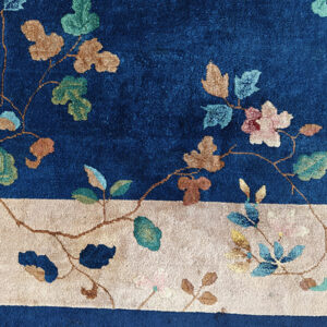 Floral rug detail showing a deep blue field meeting a wide ivory border with pink and teal elements.