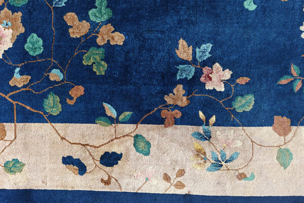 Floral rug detail showing a deep blue field meeting a wide ivory border with pink and teal elements.