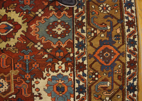 Red, blue, and brown geometric rug on a wood floor, partially covered by a dark shoe.