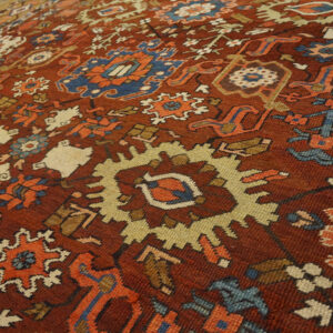 Reddish-brown rug with stylized blue, cream, and orange geometric patterns lying on wood flooring.