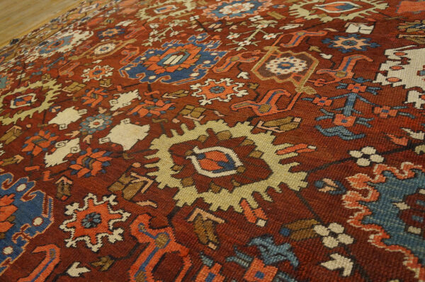 Reddish-brown rug with stylized blue, cream, and orange geometric patterns lying on wood flooring.