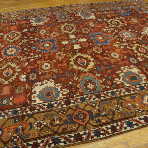 Red-brown rug with complex geometric medallions in blue, cream, and orange, displayed on hardwood flooring.