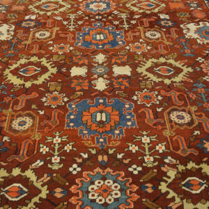 Dark red rug with dense geometric patterns in navy blue, cream, orange, and gold.