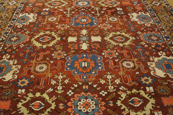 Dark red rug with dense geometric patterns in navy blue, cream, orange, and gold.