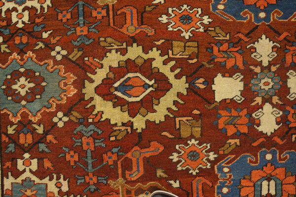 Close-up of a traditional rug with a deep rust background and geometric motifs in blue, gold, and cream.