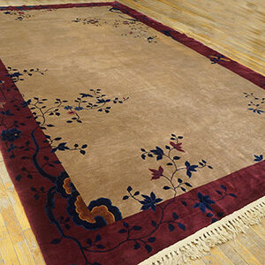 Beige area rug featuring scattered blue florals, a deep red border, and visible white fringe on wood floors.