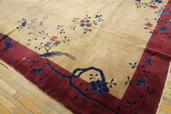 A plush tan rug with a maroon border features detailed blue and pink floral and bird designs.